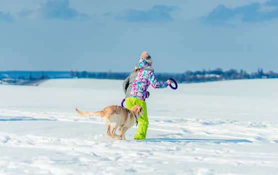 Back view of girl running in snow with dog