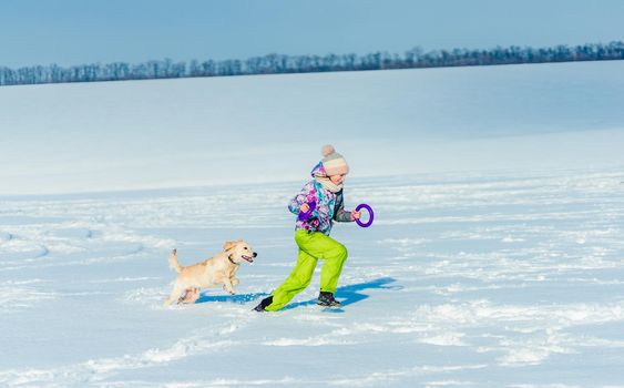 Smiling girl throwing toy ring to playful dog on winter field