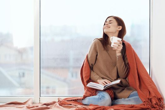 woman with a cup of drink on the windowsill reading a book rest morning. High quality photo