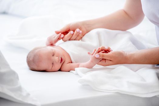 Mother holding hands of her sleeping newborn baby daughter in the bed. Parent and infant child. Family moments of matherinity