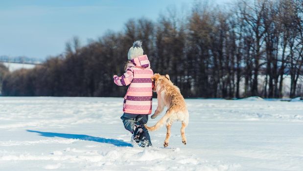 Back view of playful dog and lovely girl outside in winter