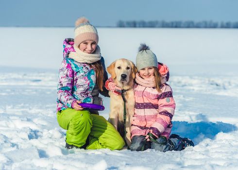 Cute sisters hugging lovely dog on sunny winter day