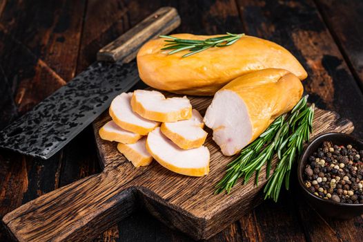 Sliced Smoked chicken breast fillet meat on a butcher board. Dark wooden background. Top view.