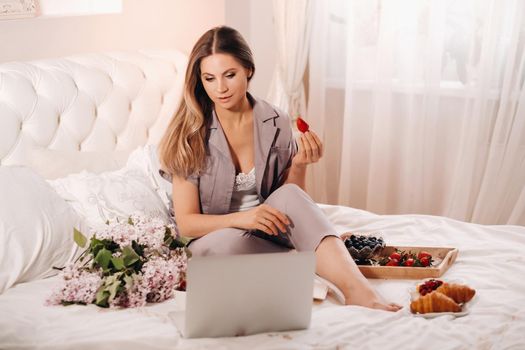 a girl sits in bed in the evening watching a laptop and eating strawberries, a girl in bed eats sweets before going to bed.