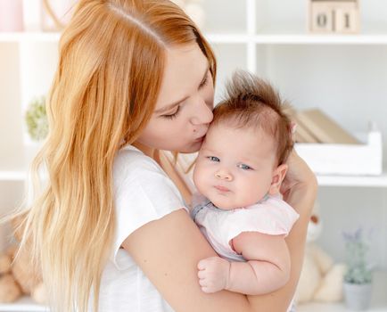 Happy mother kissing cute baby holding her up