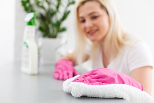 Woman in the kitchen is smiling and wiping dust using a spray and a duster while cleaning her house, close-up