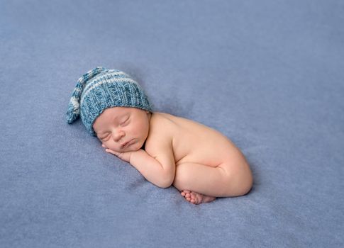 lovely naked newborn in knitted hat sleeping on gray blanket