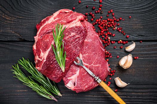 Fresh Raw Chuck eye roll beef steak on butcher table. Black wooden background. Top view.