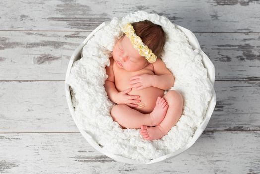 lovely sleeping bare newborn girl with headband with crossed legs in eggshell basket. top view