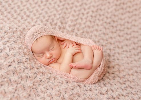 lovely newborn curled up asleep, wrapped in pink diaper on knitted blanket
