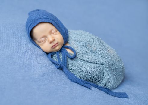 swaddled newborn boy sleeping with blue hood on his head