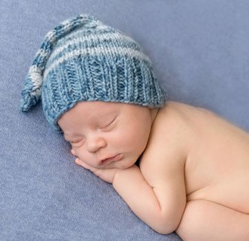 portrait of sweet sleeping newborn baby in hat covered with blanket