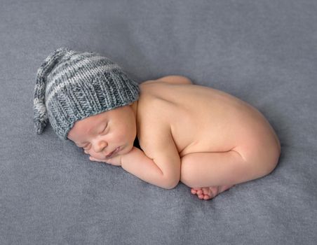 lovely naked newborn in knitted hat sleeping on gray blanket