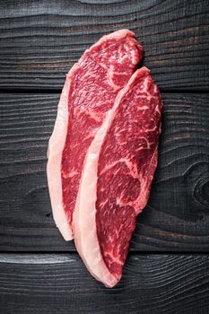 Raw rump steak or top sirloin cap beef meat steaks on butcher table. Black wooden background. Top view.