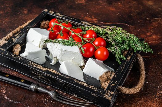 Ricotta cream Cheese in a wooden tray with basil and tomato. Dark background. Top view.