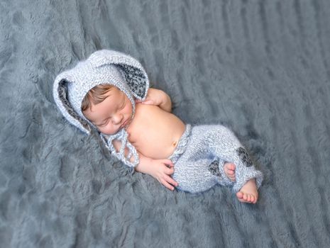 beautiful newborn baby in lovely hat with rabbit ears on furry gray blanket