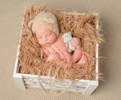 sweet sleeping newborn baby with little toy in wooden box with fluffy blaket