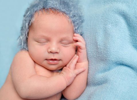 sweet newborn baby with smile sleeping on hand with blue hat on his head