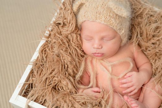 lovely newborn baby in knitted hat sleeping in wooden box with fluffy blanket