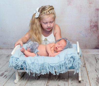 sleeping newborn boy on little bed with blue diaper and older sister watching him beside the bed