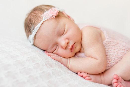 sweet face of a newborn girl with headband and flower on head sleeping on hand, close up