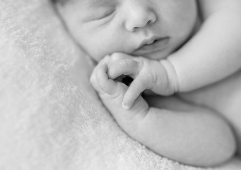 lovely sleepy face and hands with crossed fingers of a newborn baby, black and white photo, close up