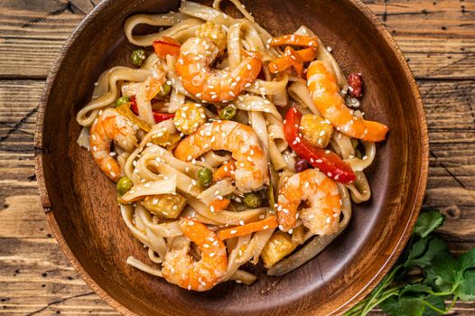 Udon stir-fry noodles with shrimp prawns in a wooden bowl. wooden background. Top view.