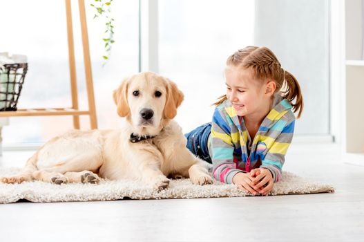Happy school girl with calm young retriever dog lying at home