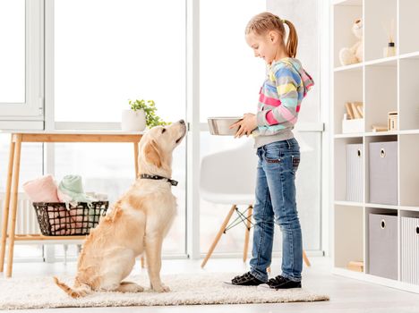 Beautiful little girl feeding cute dog indoors