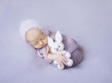 swaddled sleeping newborn girl with white toy in hand