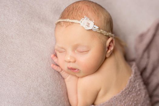 lovely sleeping newborn girl with flower on her headband with hand under her head