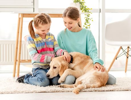 Happy sisters cuddling cute dog sitting on floor at home