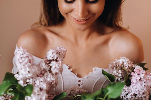 Beautiful girl with lilac flowers in her hands. A girl with lilac flowers in the spring at home. A girl with long hair and lilac in her hands.