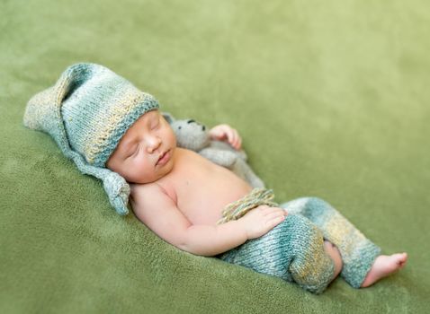 lovely newborn baby in knitted hat and panties sleeps curled up, top view