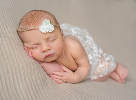 sweet newborn girl sleeping on her hand with flowers on headband