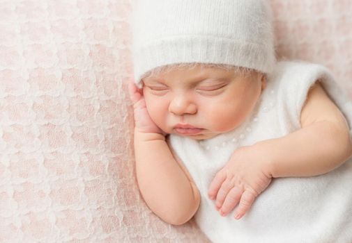 lovely sleeping newborn girl with sweet cheeks in white hat and suit