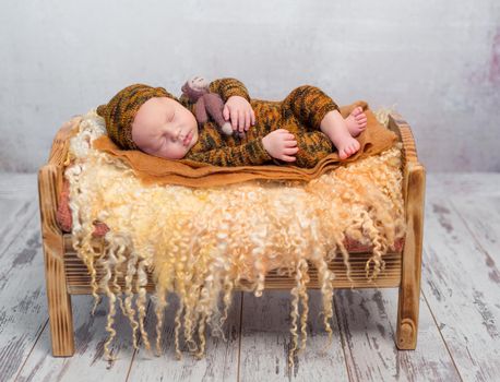 sleeping newborn boy in hat and suit on little bed with fluffy blanket