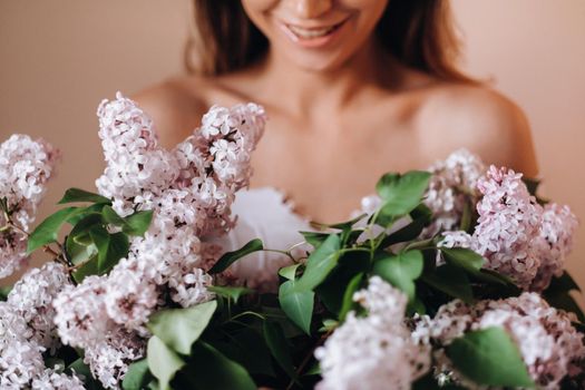 Beautiful girl with lilac flowers in her hands. A girl with lilac flowers in the spring at home. A girl with long hair and lilac in her hands.