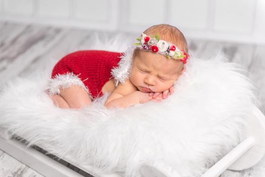 lovely newborn girl in red romper and colorful headband sleeping on white fluffy blanket