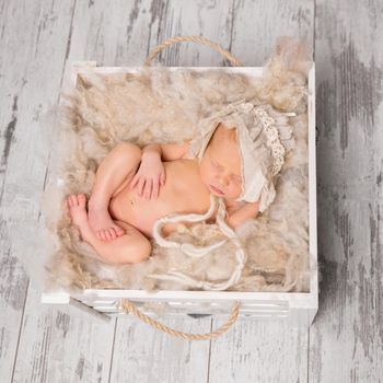 cute naked baby with hat sleeping in box on wooden background