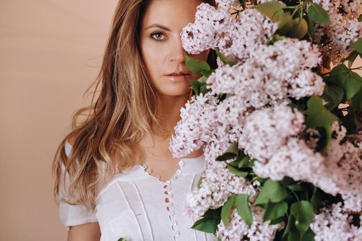 Beautiful girl with lilac flowers in her hands. A girl with lilac flowers in the spring at home. A girl with long hair and lilac in her hands.