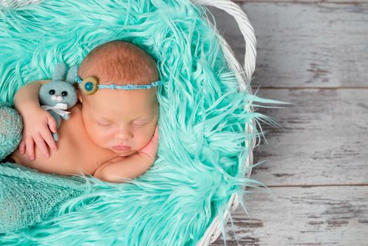 sweet sleeping newborn girl on turquoise fluffy blanket with flowers on her headband
