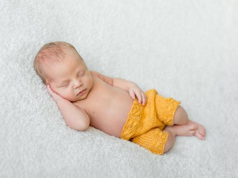 sweet sleeping newborn boy in yellow panties with head on his hand