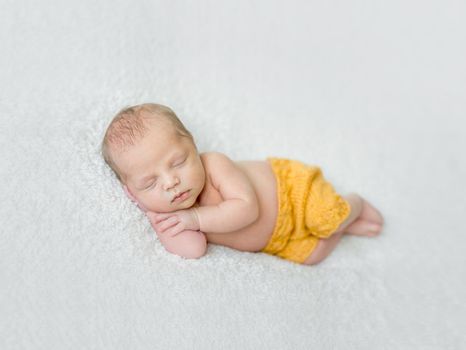 sweet sleeping newborn boy in yellow panties with head on his hand