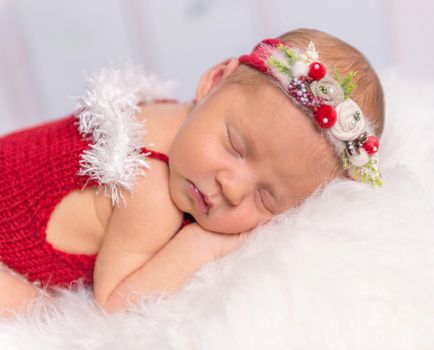 lovely newborn girl in red romper and colorful headband sleeping on white fluffy blanket