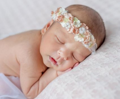 funny sleeping newborn girl with her hands under her head and headband with flowers