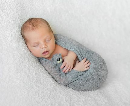 wrapped in gray diaper sleeping baby with opened mouth holding little toy