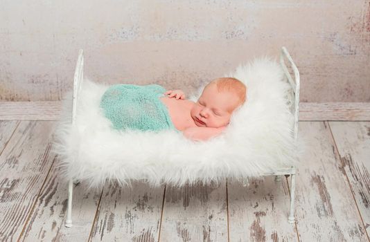 lovely wrapped newborn sleeping on cot with white soft blanket and toy