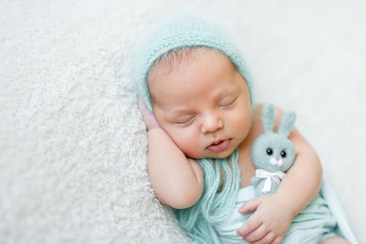 lovely sleeping baby with blue hat, panties and toy on white blanket close up
