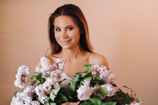 Beautiful girl with lilac flowers in her hands. A girl with lilac flowers in the spring at home. A girl with long hair and lilac in her hands.